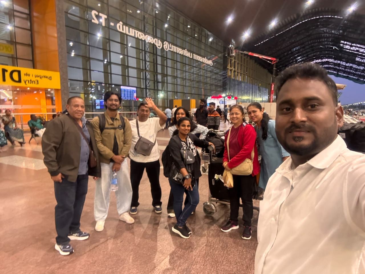 Group of eight travellers with luggage trolleys outside Chennai airport Terminal 2 at night