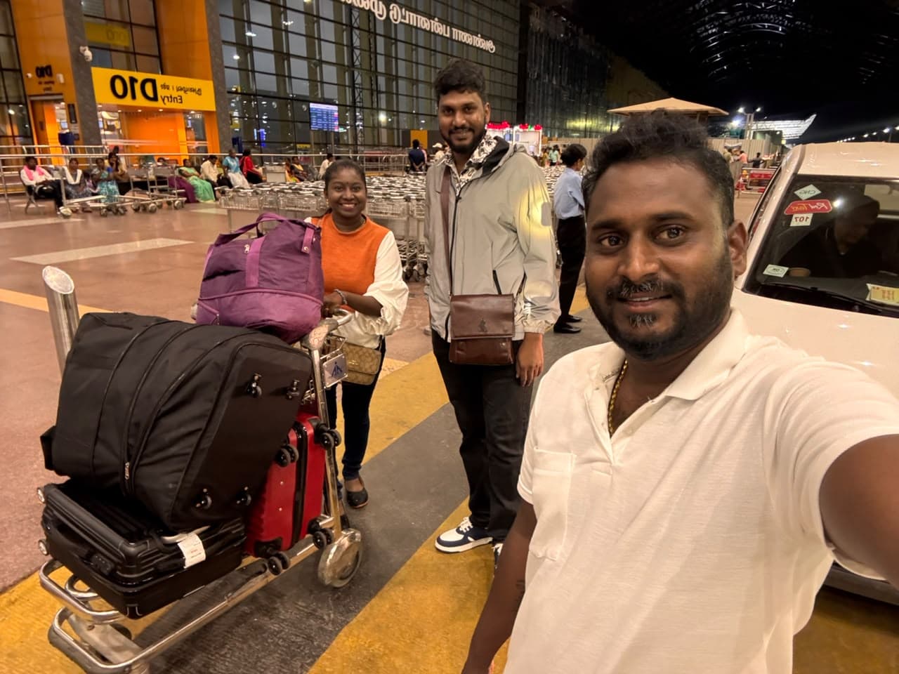Two travellers with a loaded luggage trolley beside the car at Chennai airport before a Kerala trip
